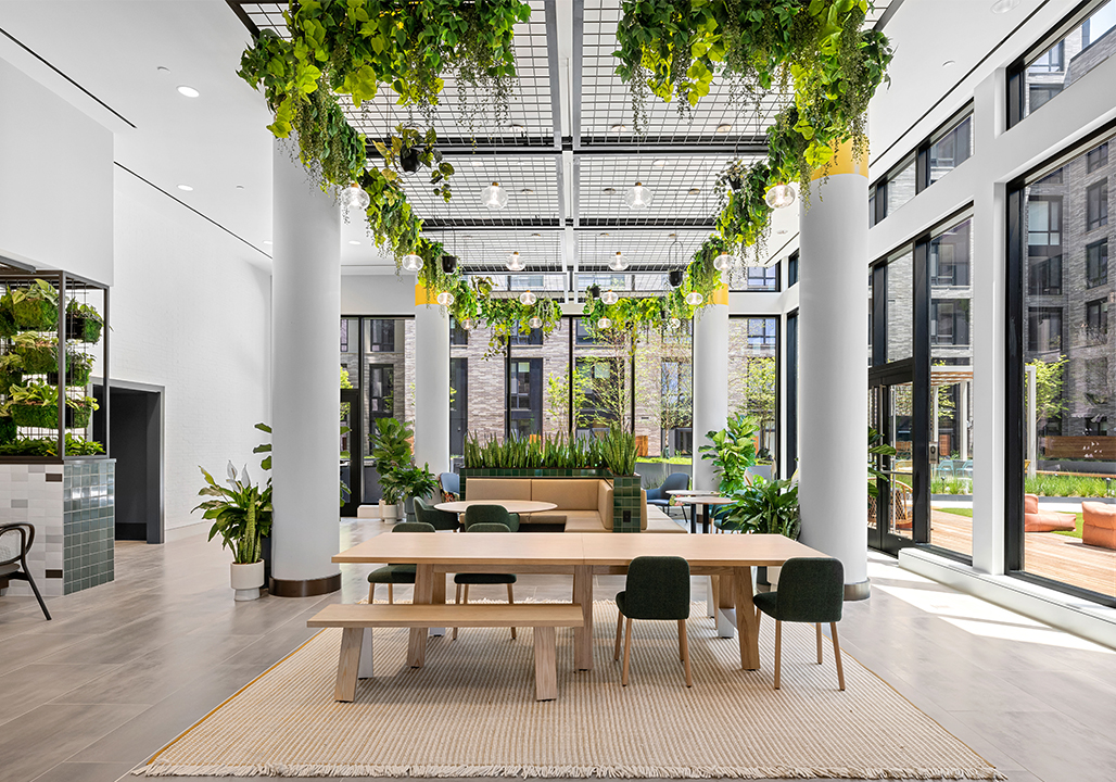 Greenhouse-inspired lounge with hanging greenery, seating and tables, and large windows