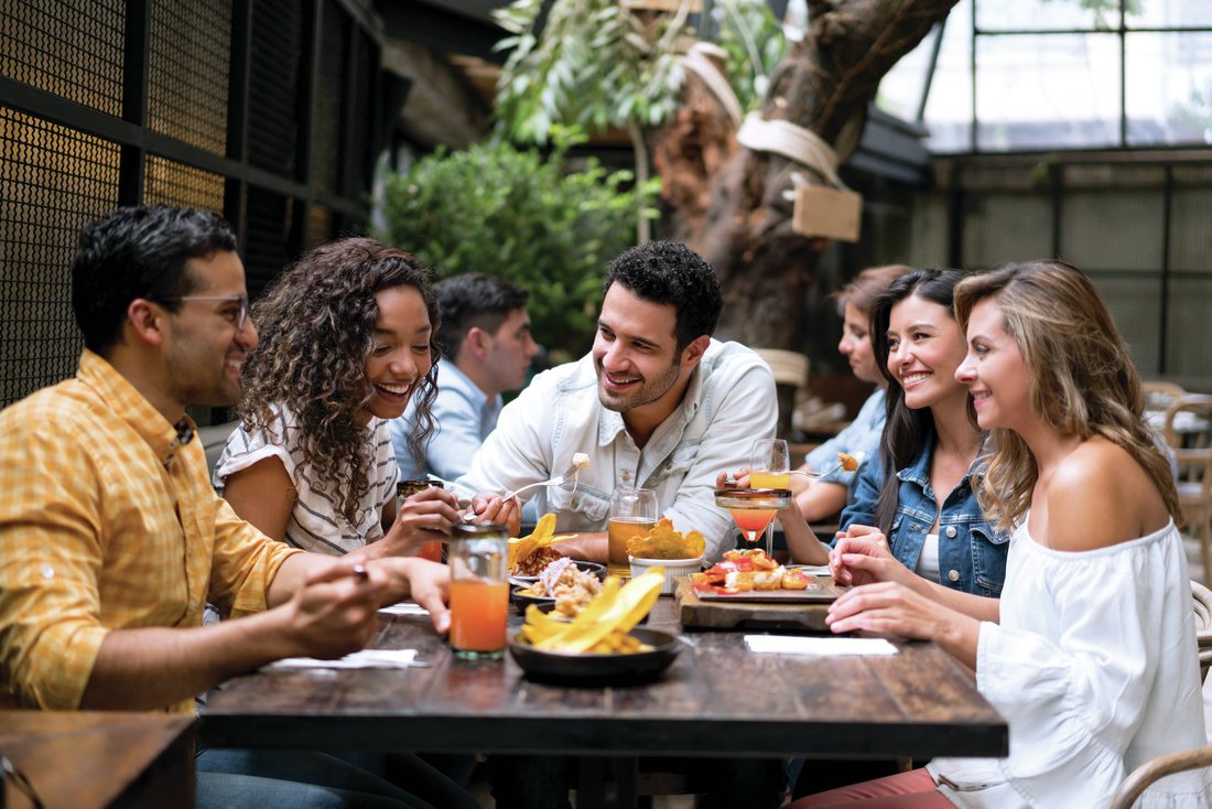 Group of five diverse individuals enjoying food and drinks around a wood table at a hip restaurant